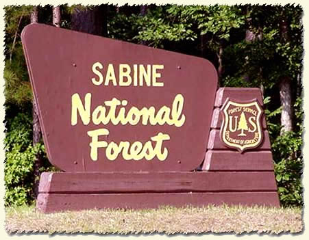 A sign for Sabine National Forest featuring the US Forest Service emblem, set against a wooded background.