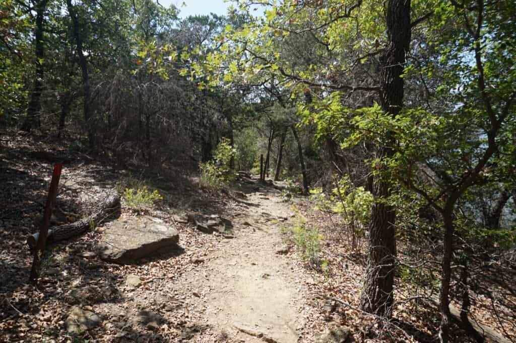 Lake Mineral Wells State Park A rocky dirt trail through oak woods along the lake, with a red trail marker post