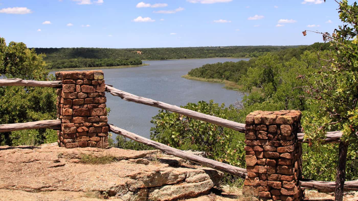 Stone pillars and a rail fence at an overlook above Lake Mineral Wells, with wooded hills around the lake